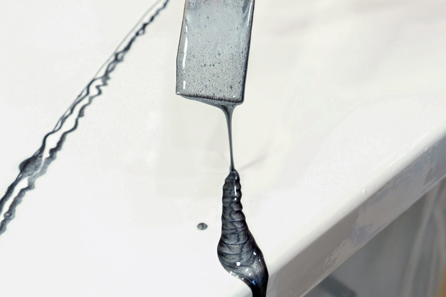 A close-up of a gray paint being poured from a spatula onto a white surface.