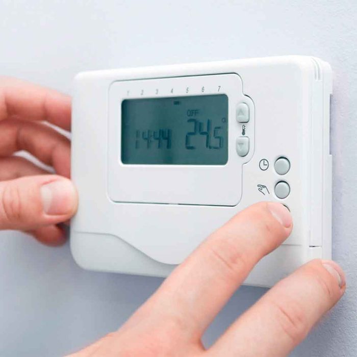 A hand adjusts a digital thermostat on a wall, displaying the current temperature as 24.5°C amid a simple interior setting.