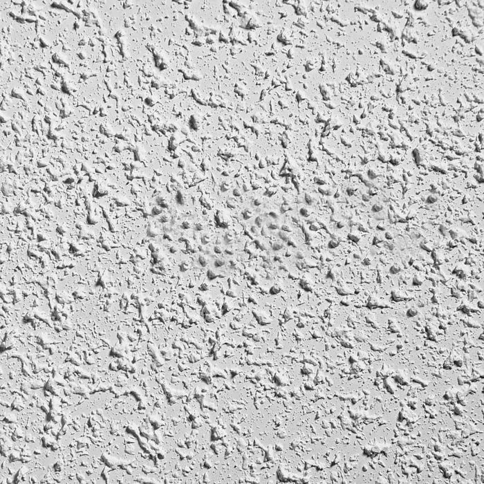 A textured white wall surface displays uneven patterns, with small bumps and grooves creating a three-dimensional effect in a softly lit environment.