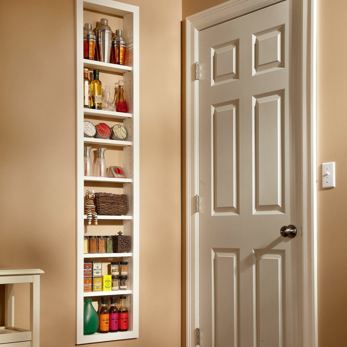 A narrow white shelf displays various bottles, jars, and decorative items against a beige wall, next to a closed white door.