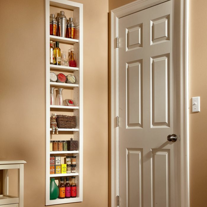 A narrow white shelf displays various bottles, jars, and decorative items against a beige wall, next to a closed white door.
