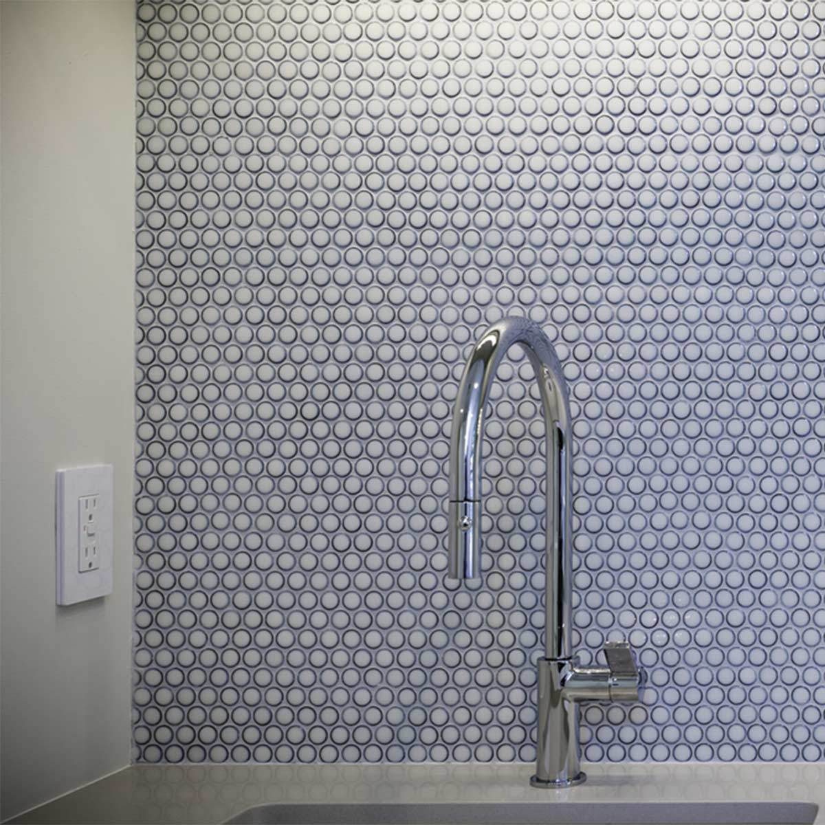 A sleek chrome faucet stands against a textured, circular-patterned wall in a modern kitchen, emphasizing a clean and contemporary design aesthetic.