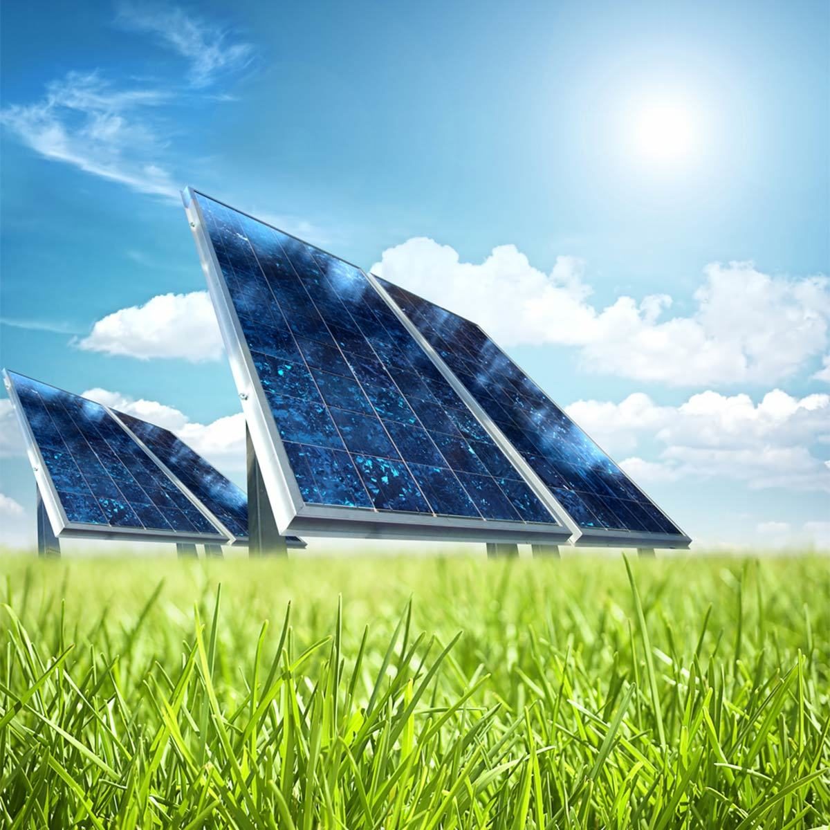 Solar panels capture sunlight, converting it into energy. They are positioned on a grassy field under a bright blue sky with scattered clouds.