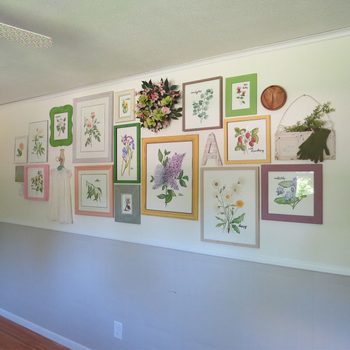 A wall showcases various framed botanical art pieces and a decorative wreath, enhancing the bright, airy ambiance of the room.