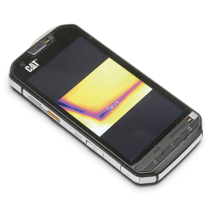 A rugged smartphone displays a colorful thermal image with temperature readings, resting on a flat surface, designed for durability in tough environments.