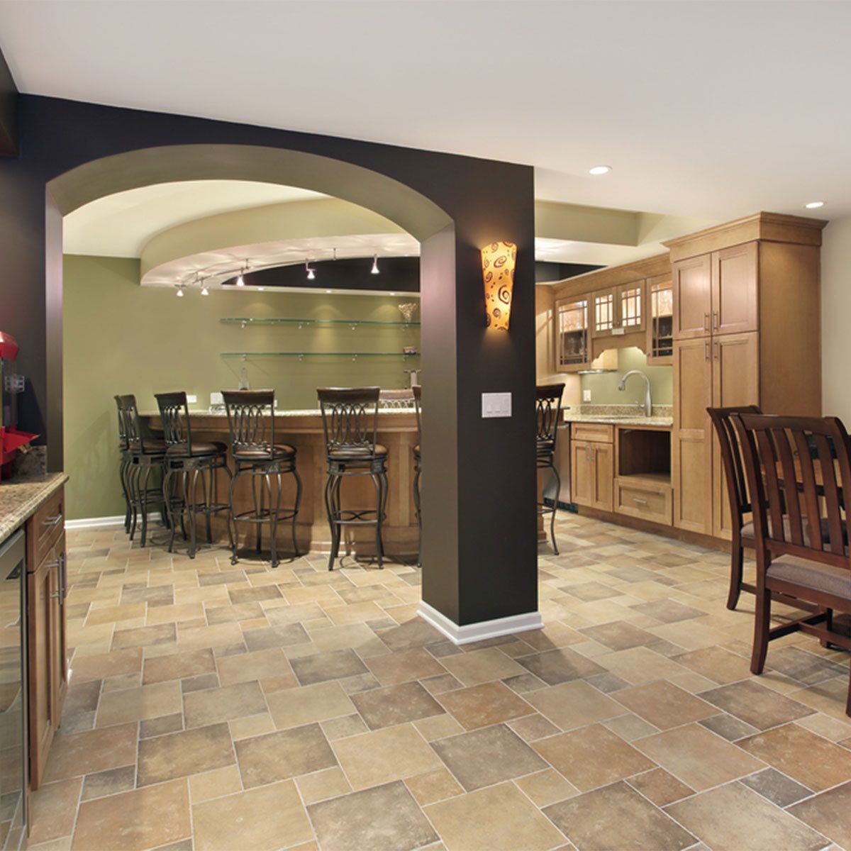 A modern kitchen features a bar area with tall chairs, surrounded by beige and brown tiled flooring, and warm lighting highlighting wooden cabinetry.