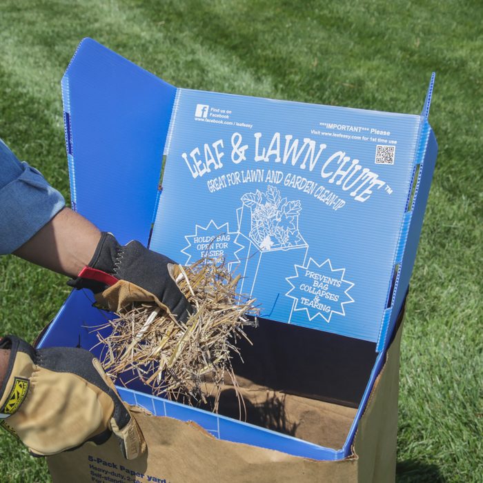 A hand holding dried leaves and grass is placing them into a blue container labeled 