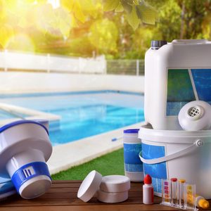 Containers for pool maintenance sit on a wooden surface. They are surrounded by a clear pool and green lawn, basking in sunlight.