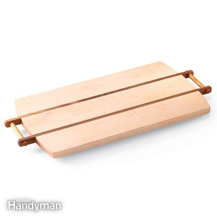 A wooden cutting board with two handles resting horizontally on a flat surface, allowing for easy lifting and maneuvering.