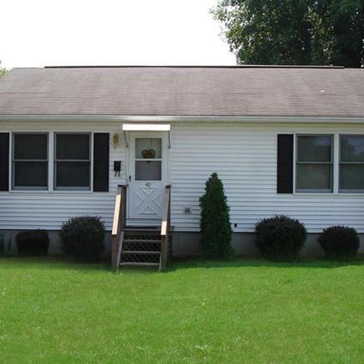 A small white house stands on a green lawn. A set of stairs leads up to a central door, flanked by windows.