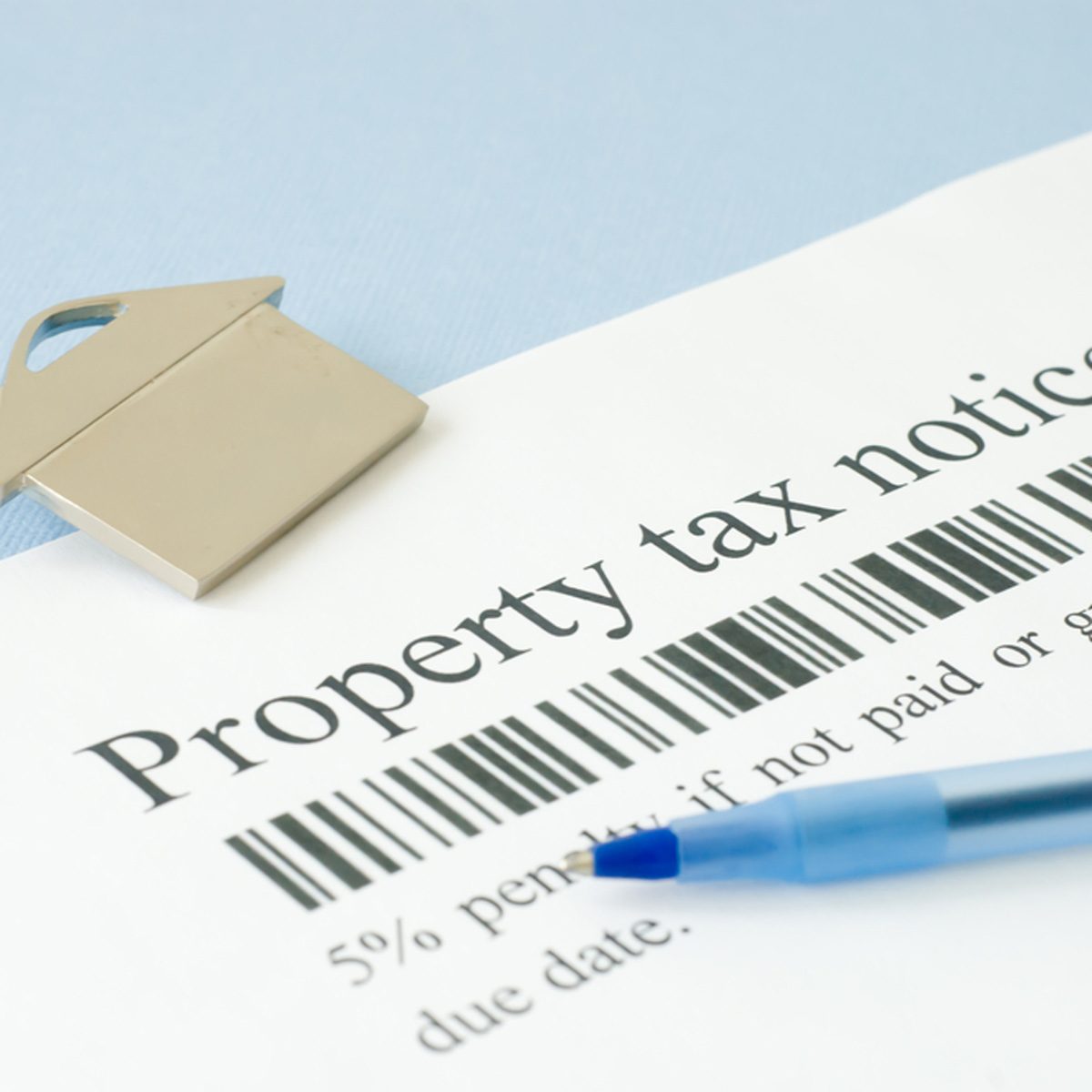 A metallic key shaped paperweight rests on a property tax notice, while a blue pen lies nearby, suggesting preparation for payment.