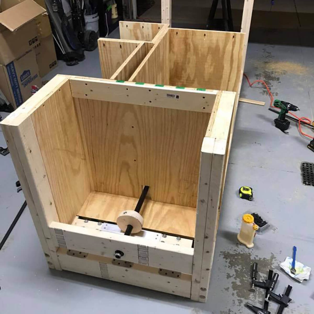 A partially constructed wooden frame sits on a work surface, surrounded by tools and materials, indicating a project in progress in a workshop.