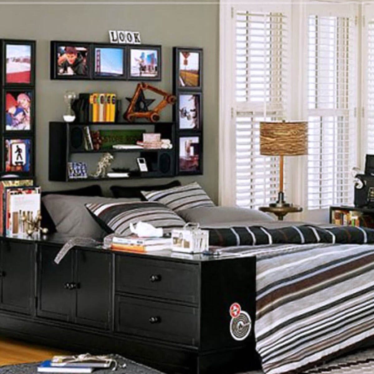 A neatly made bed with striped bedding sits in a room featuring framed photos on the wall, shelves with decor, and a lamp next to the window.