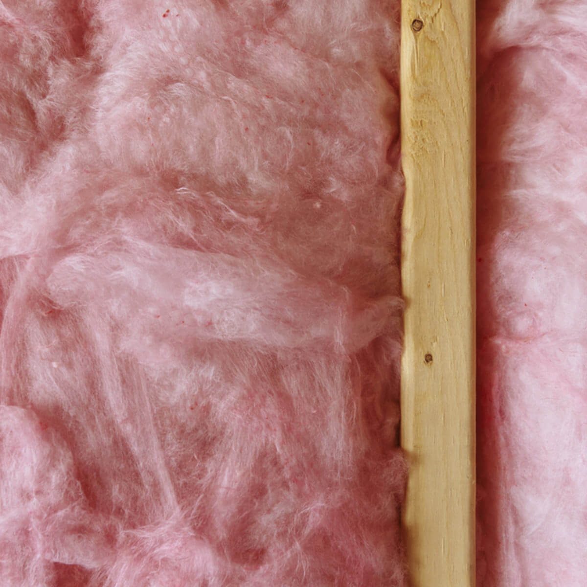 Insulation material covers a surface, with a wooden plank vertically positioned beside it, creating a textured, pink backdrop in a construction or renovation setting.