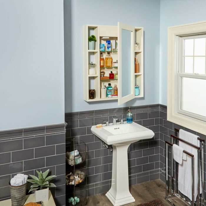 A bathroom features a white sink and a mirrored cabinet with open doors displaying toiletries, alongside a window and neatly arranged towels.