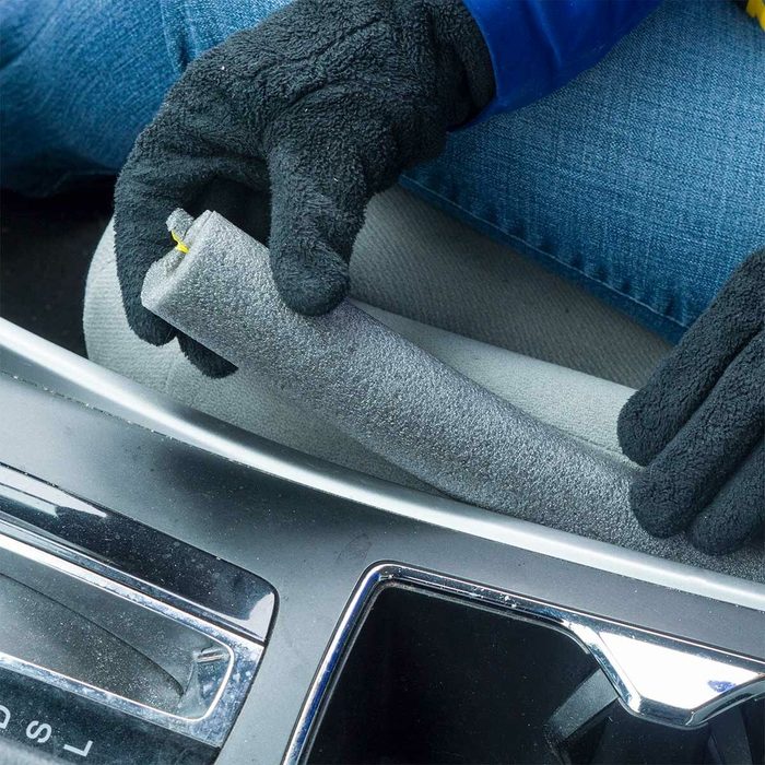 A gloved hand holds a gray foam roller, positioned near a car