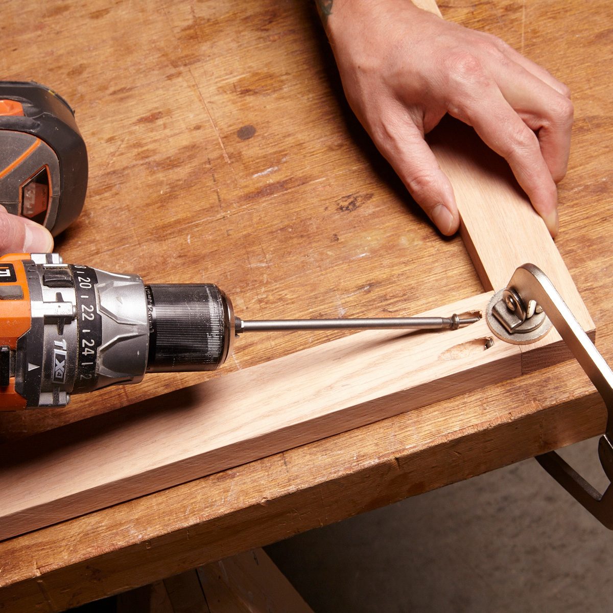 A drill is driving a screw into wooden pieces on a workbench, while a hand holds a clamp nearby for stability. Assemble the face frame with pocket hole screws.