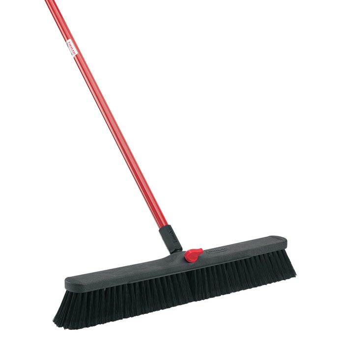 A red-handled broom with a wide black bristle head stands upright, ready for use in sweeping floors or surfaces clean.