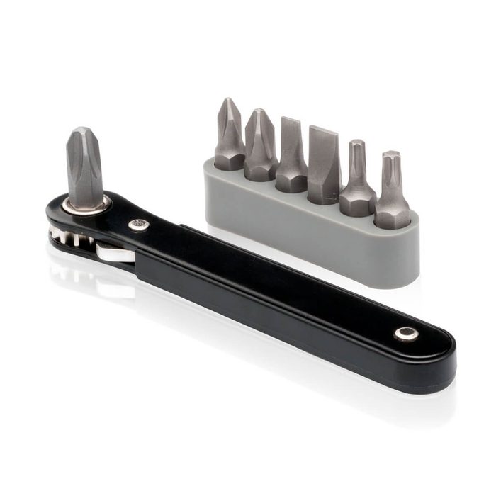 A black ratchet handle with a bit attached is placed next to a gray holder containing six metal bits, suitable for various screw types.