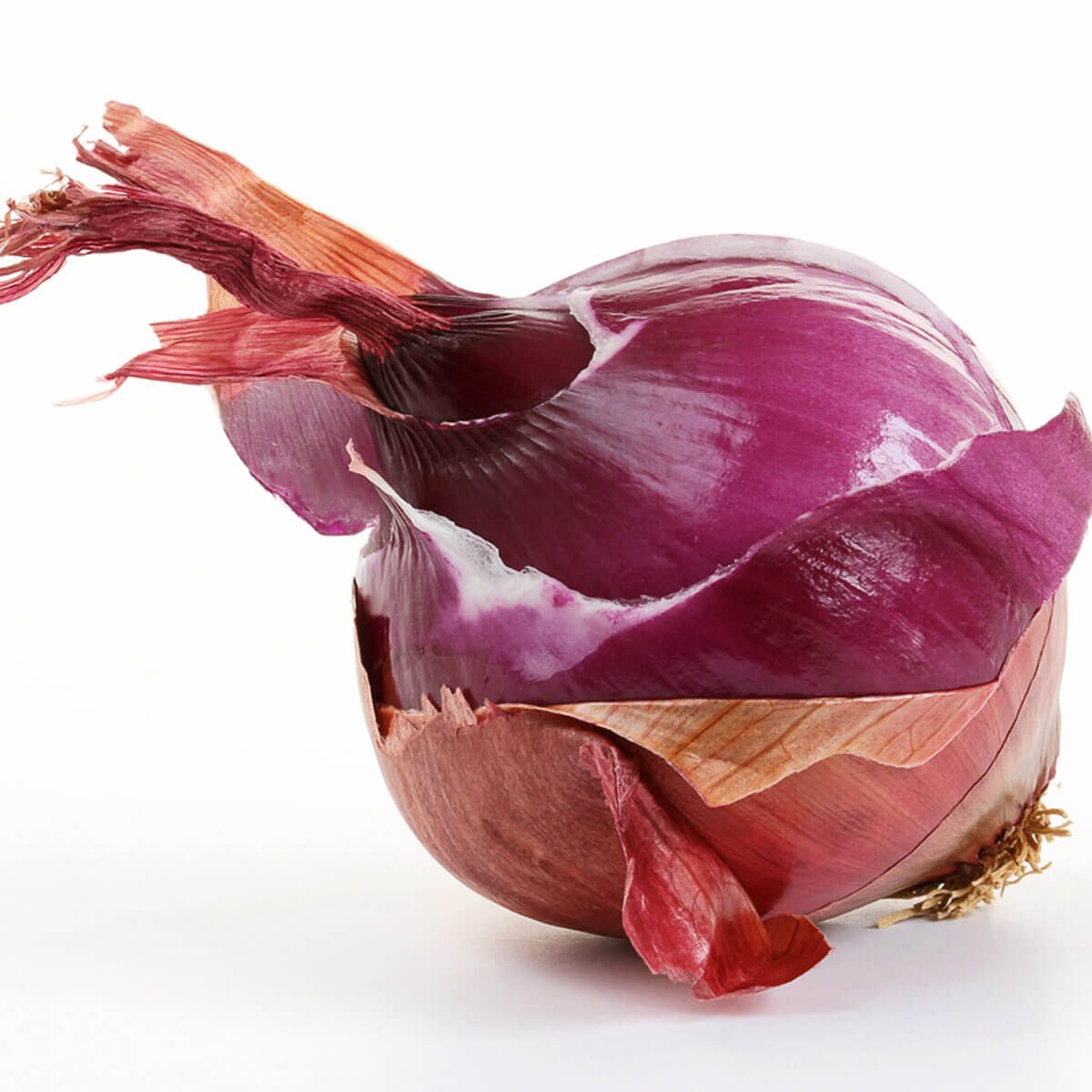 A red onion rests on a white surface, partially revealing its layers while displaying wrinkled, vibrant skin, highlighting its natural shape and texture.