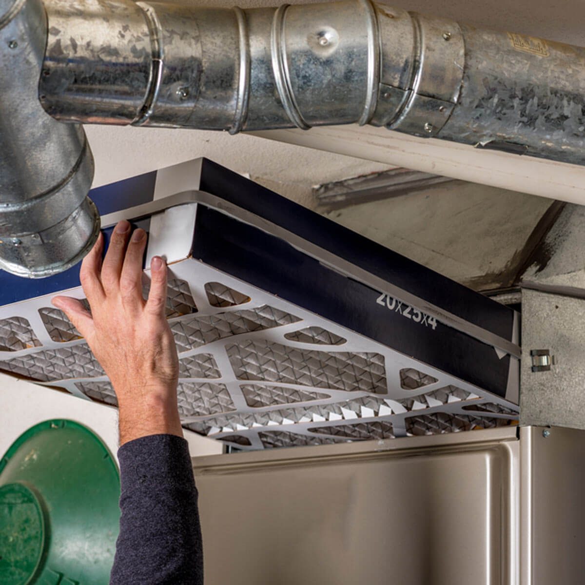 A hand installs an air filter into a metallic duct system, surrounded by industrial elements in a dimly lit space.