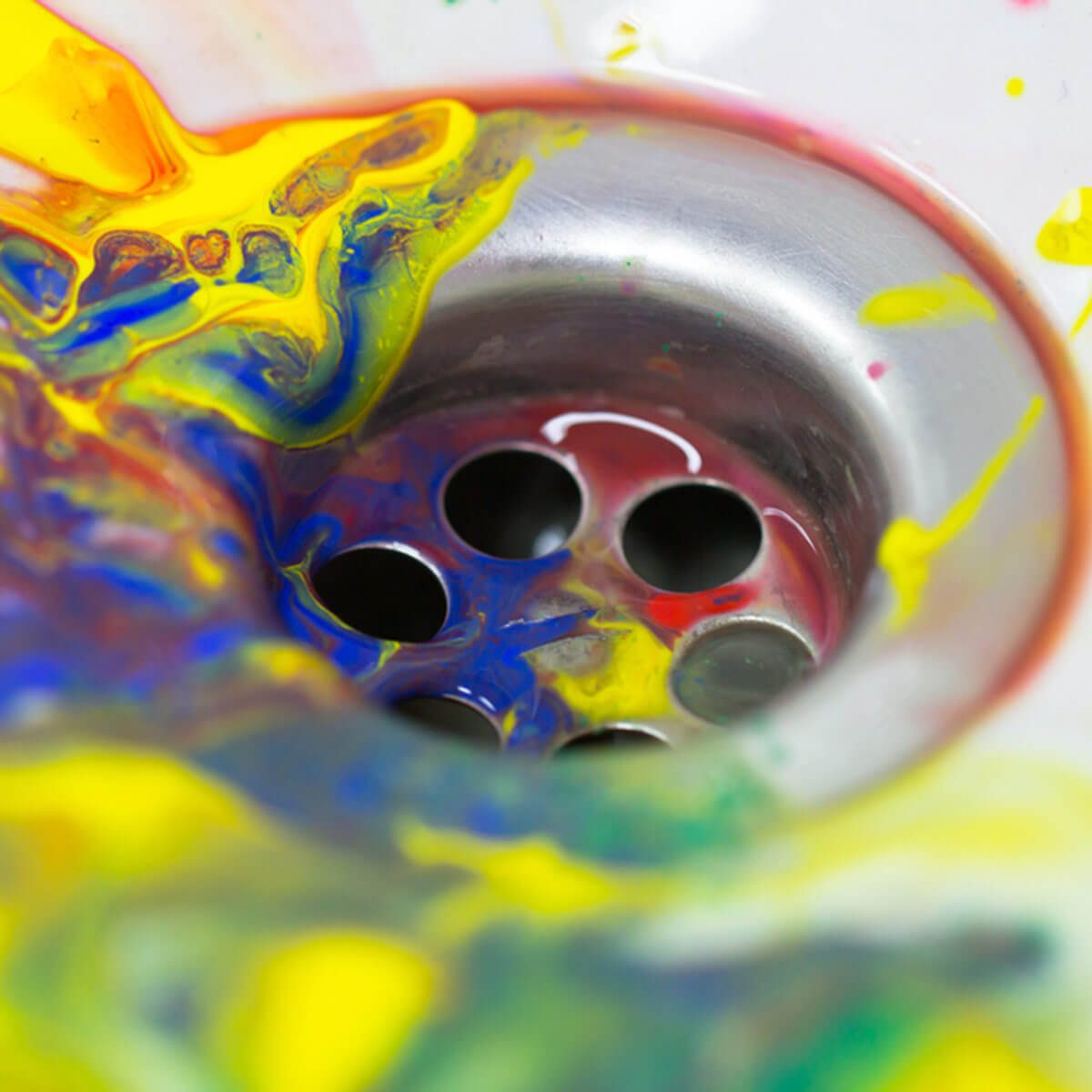 A metallic drain is surrounded by swirling, vibrant colors of paint. The paint flows around the drain, creating a chaotic and colorful scene.