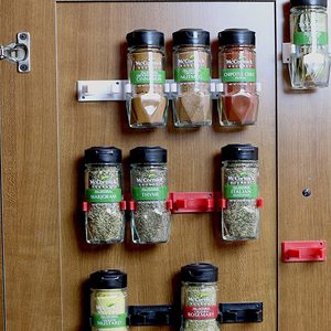 Glass spice jars are mounted on a wooden surface, displaying various spices. The jars are organized in two rows, secured with clips for easy access.