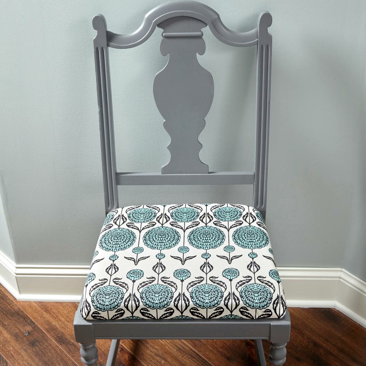 A gray wooden chair with a floral-patterned seat rests against a light green wall, positioned on a wooden floor.