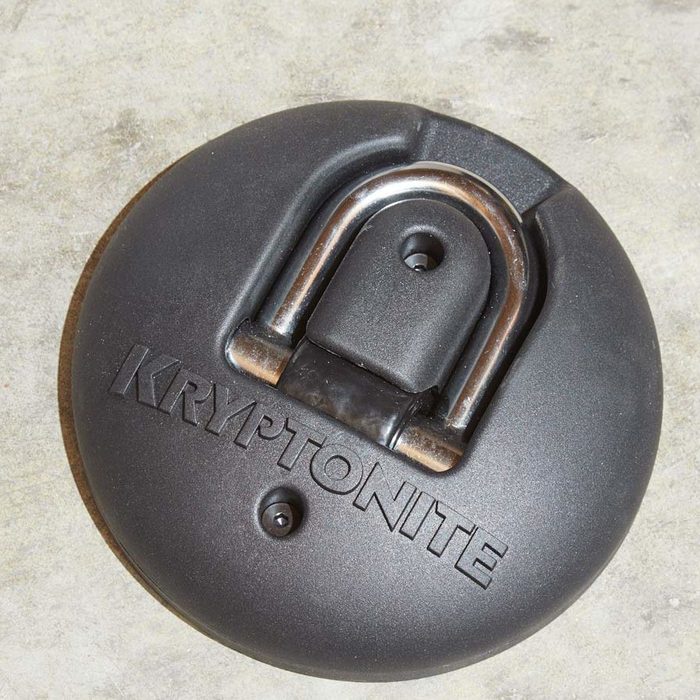 A round black lock sits on a gray concrete surface, featuring a metallic shackle and the engraved word 