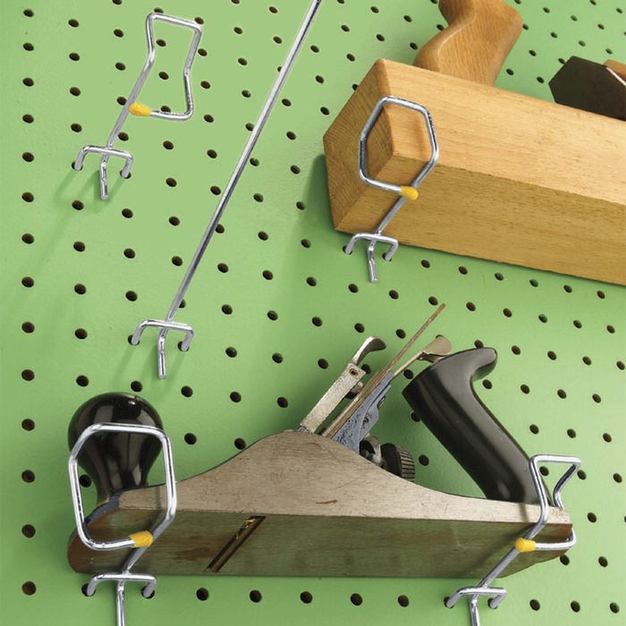 Tools are hanging on a green pegboard, secured with metal hooks. A wooden block and a hand plane are prominently displayed among various tools.