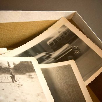 Several black-and-white photographs are arranged haphazardly in a light-colored box, showcasing various scenes and capturing moments from the past.