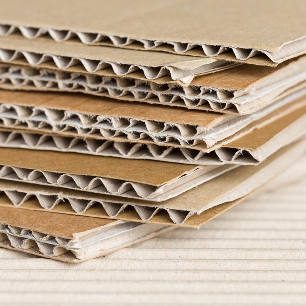Layers of corrugated cardboard are stacked neatly, showcasing their textured surface and structural design against a flat, textured background.
