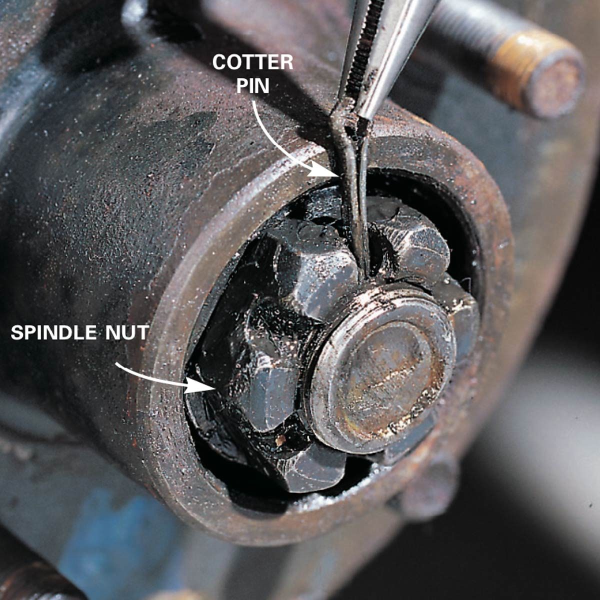 A rusty spindle nut is being removed with a pair of pliers, revealing a cotter pin in a mechanical setting.