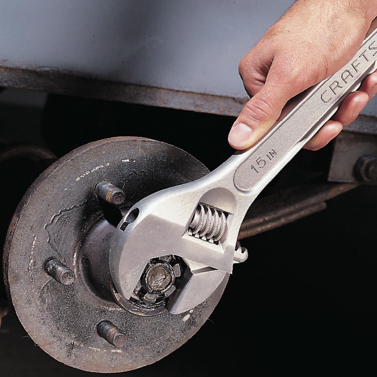 A hand grips an adjustable wrench, turning a bolt on a wheel hub in a dimly lit workshop environment.