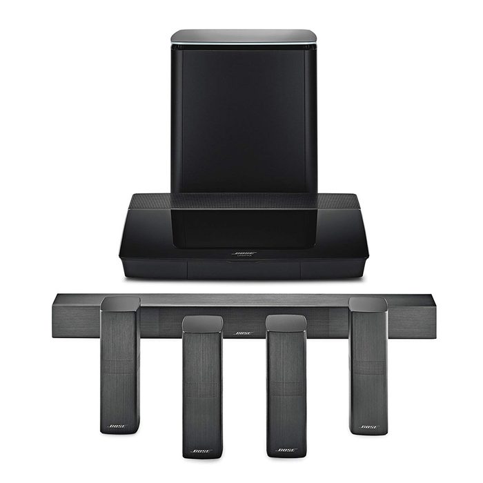 A black audio system includes a central soundbar and three satellite speakers, designed for home theater use, arranged neatly in a compact formation.