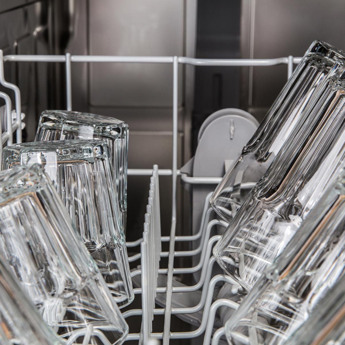 Transparent glasses are positioned upside down in a dishwasher's rack, being prepared for cleaning in a stainless steel environment.
