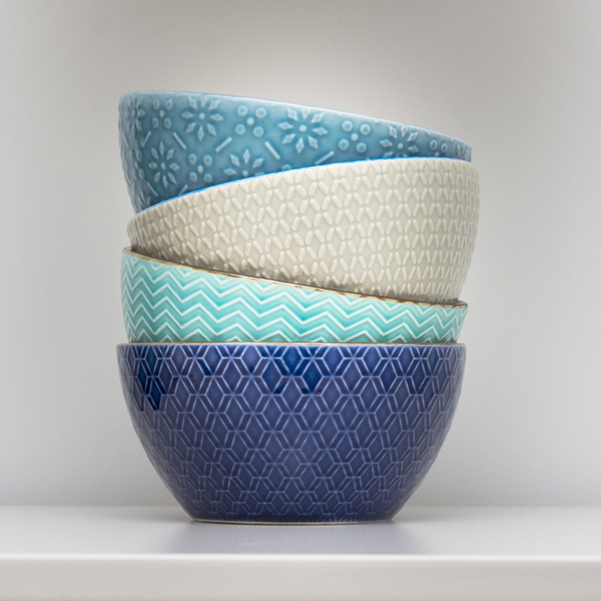 Five stacked bowls display various textured patterns and colors, resting on a flat surface against a plain backdrop.