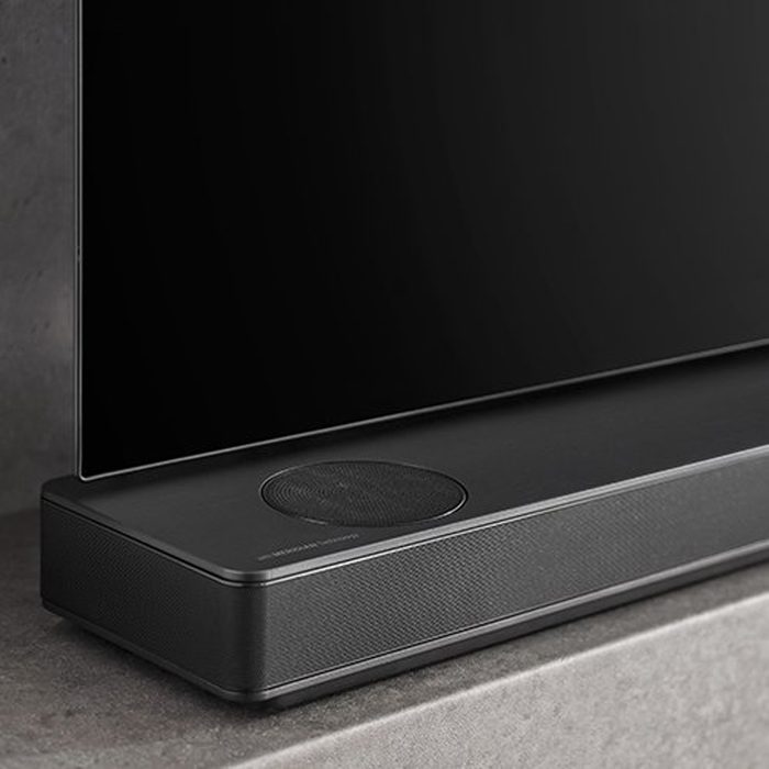 A sleek black television rests on a stone surface, with a visible speaker and microphone embedded in its base, blending modern design with functionality.