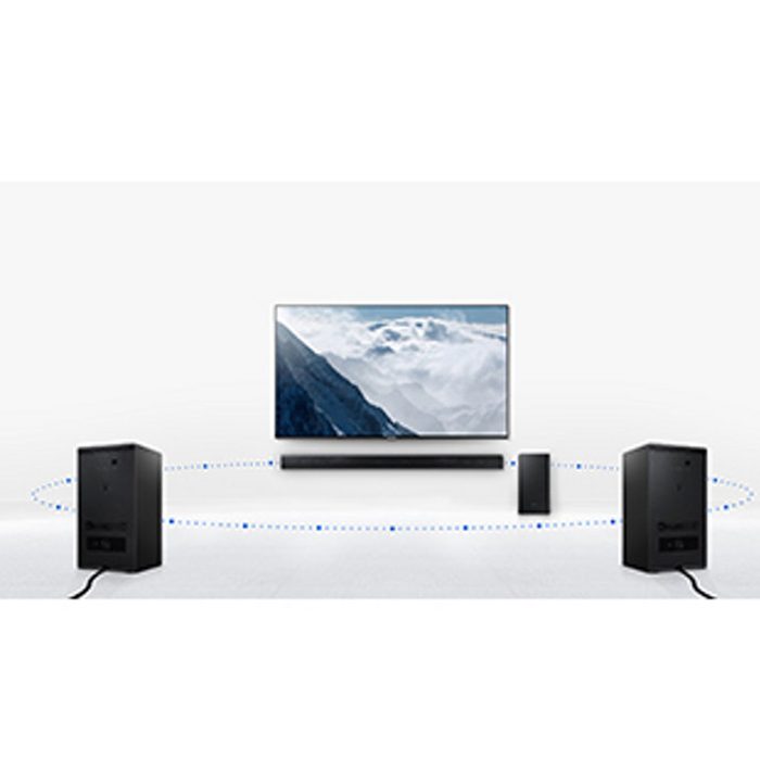 A television displays a mountainous landscape while a soundbar and two black speakers surround it, creating a home theater setup in a minimalistic environment.