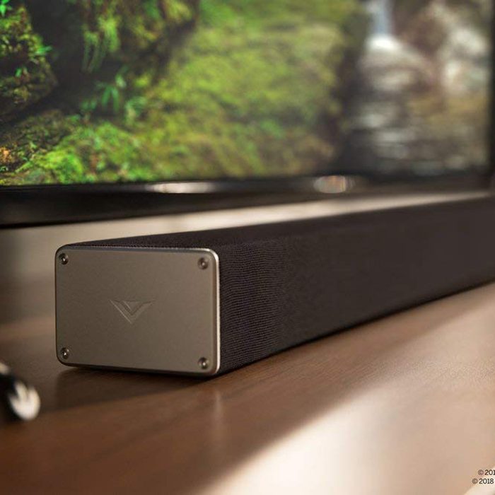 A sleek black soundbar sits on a wooden surface, complementing a nearby television displaying a vibrant nature scene.