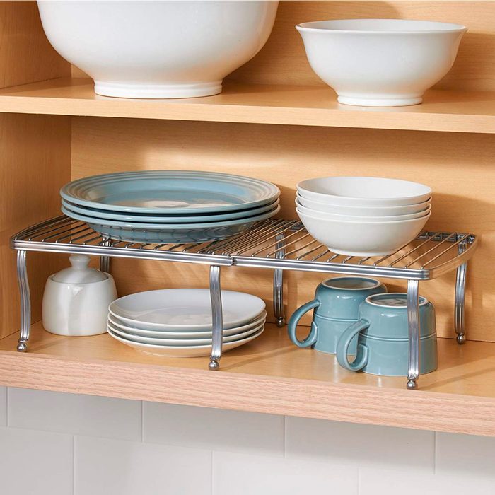 A metal shelving unit holds various dishes, including blue plates and white bowls, arranged neatly on a wooden kitchen shelf.