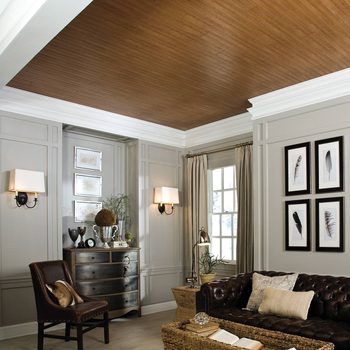 A brown leather sofa sits in a well-lit room, surrounded by framed artwork, a wooden ceiling, and decorative furnishings, creating a cozy atmosphere.