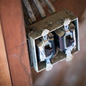 Two dusty light switches are mounted on a wall, with electrical wires connected above them, indicating an older, potentially unused electrical system.