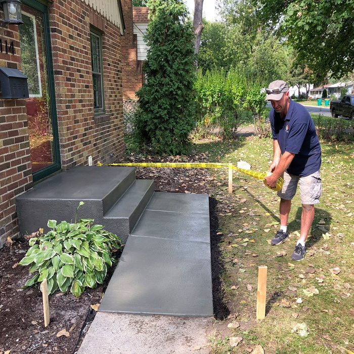 Man placing a tape barricade around a new concrete step | Construction Pro Tips