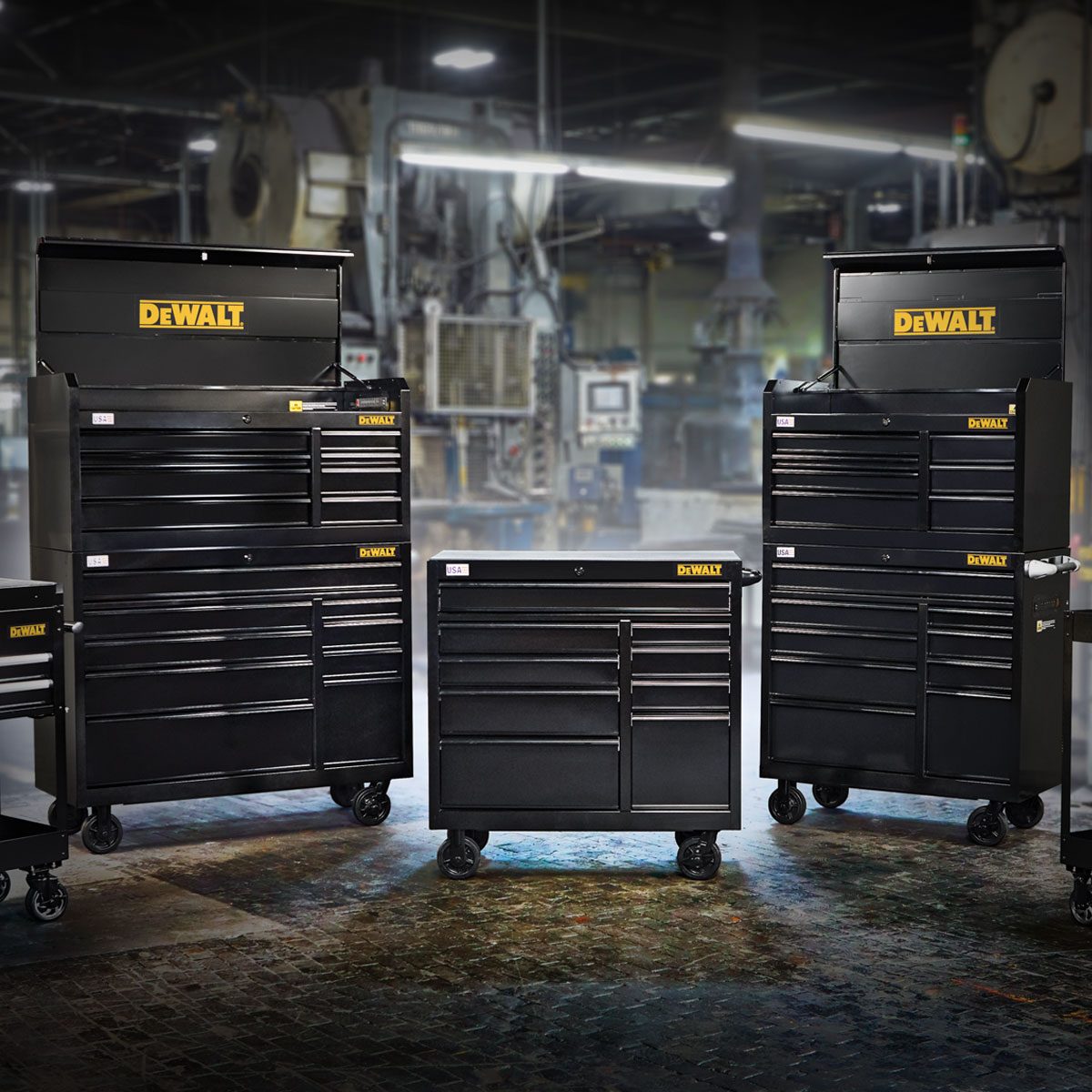 Four black tool chests are arranged prominently, showcasing drawers and features, set against an industrial backdrop with machinery.