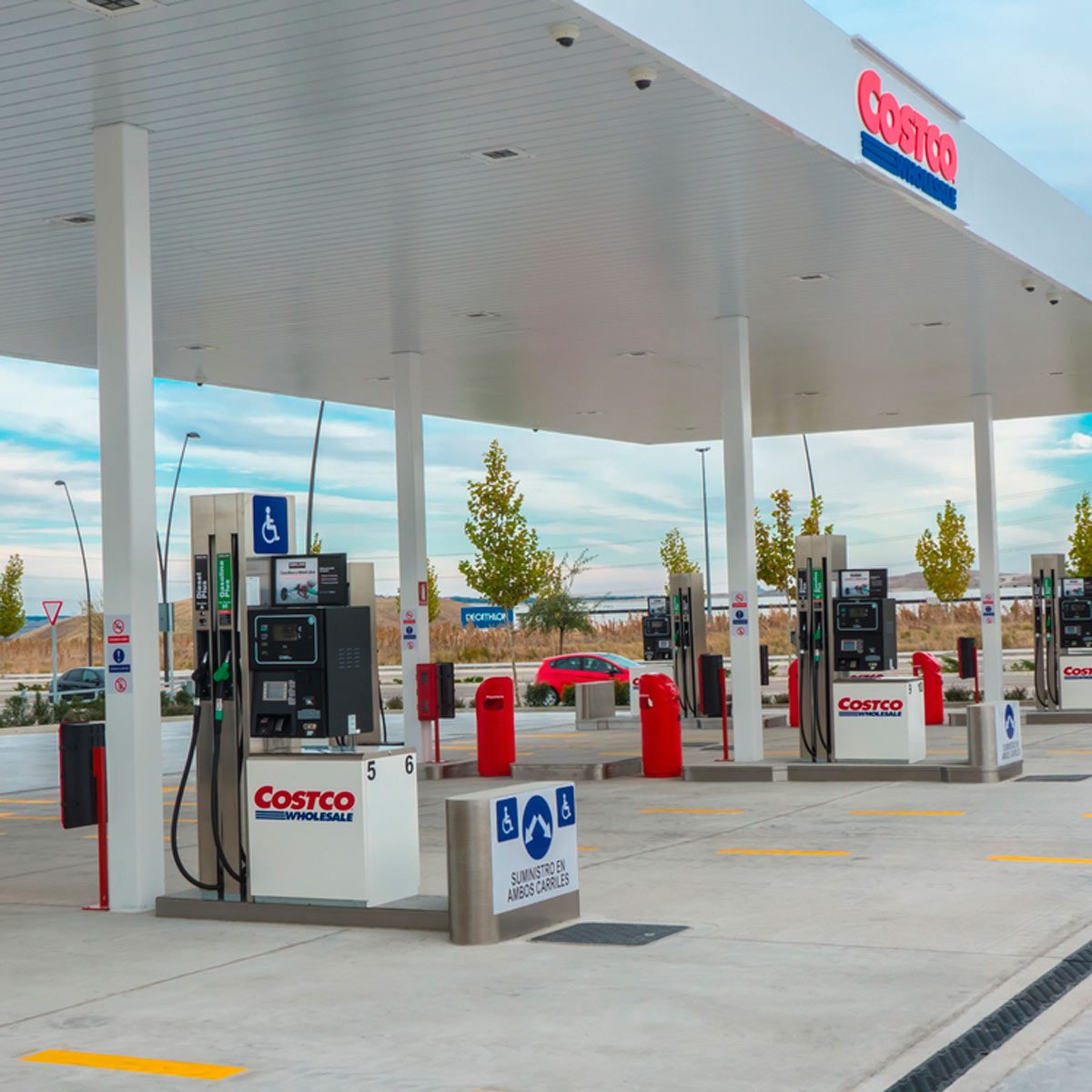Gas pumps are arranged at a Costco station, serving vehicles under a large canopy, with trees and a clear sky in the background.