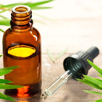 An amber glass bottle with a dropper sits on a wooden surface, surrounded by green leaves, suggesting a natural or herbal product.
