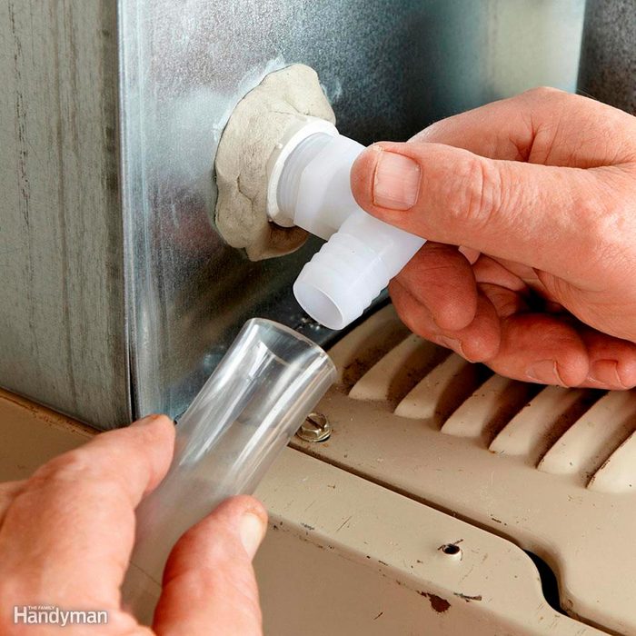 A person connects a clear plastic tube to a white fitting on a metal surface, surrounded by beige machinery components.