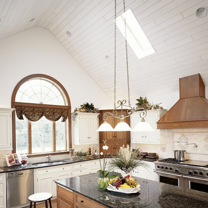 A kitchen features a central island with a fruit bowl, pendant lights hanging above, and large windows letting in natural light amid elegant cabinetry.