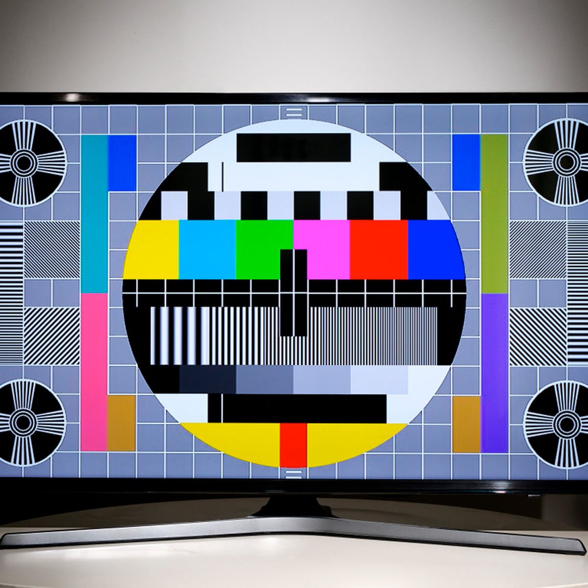 A television displays a color test pattern with geometric shapes and various colors against a gray background, indicating it is not broadcasting content.